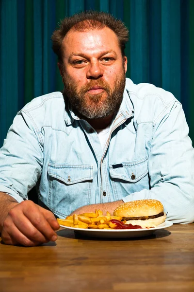 ファーストフードの食事を食べることのひげを持つ男。フライド ポテトとハンバーガーを楽しむ. — ストック写真