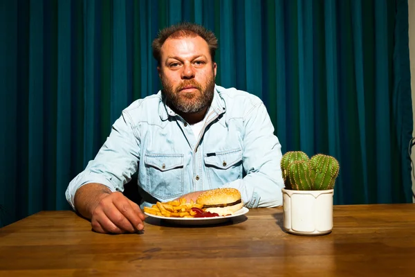 Hombre con barba comiendo comida rápida. Disfrutando de papas fritas y una hamburguesa . — Foto de Stock