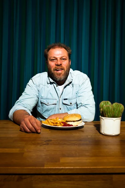 Άνθρωπος με γένια τρώνε γεύμα fast food. απολαμβάνοντας τις πατάτες τηγανιτές και ένα χάμπουργκερ. — Φωτογραφία Αρχείου