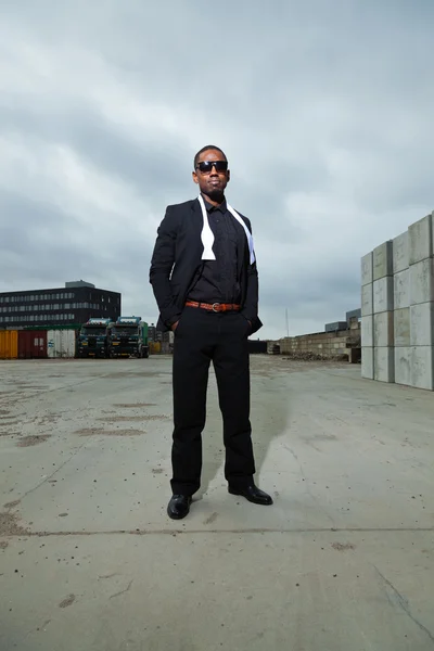 Hombre americano negro fresco en traje oscuro con gafas de sol. Foto de moda en entorno urbano . —  Fotos de Stock