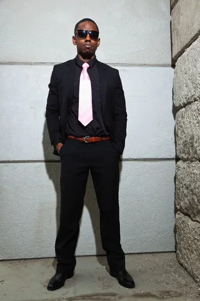 Um americano negro fixe de fato escuro a usar óculos escuros. Moda tiro em ambiente urbano . — Fotografia de Stock