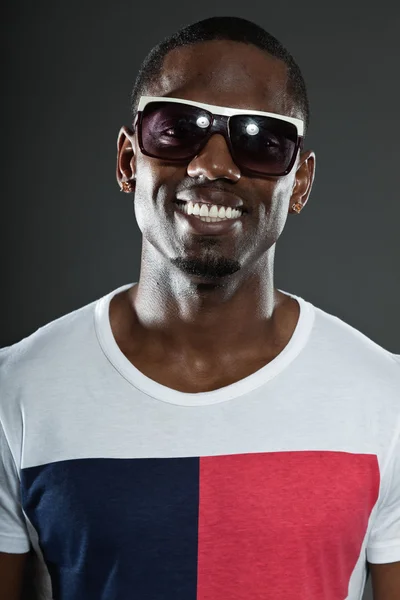 Cool urban stylish black american man. Fashion studio portrait isolated on grey background. Wearing dark sunglasses. Smiling. — Stock Photo, Image