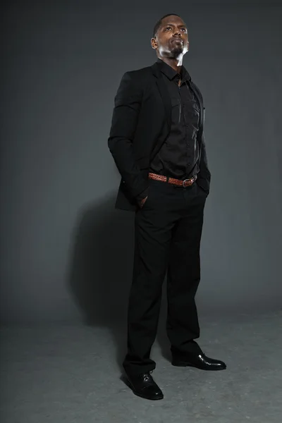 Cooler schwarzer amerikanischer Mann im dunklen Anzug. Ateliermode isoliert auf grauem Hintergrund aufgenommen. — Stockfoto