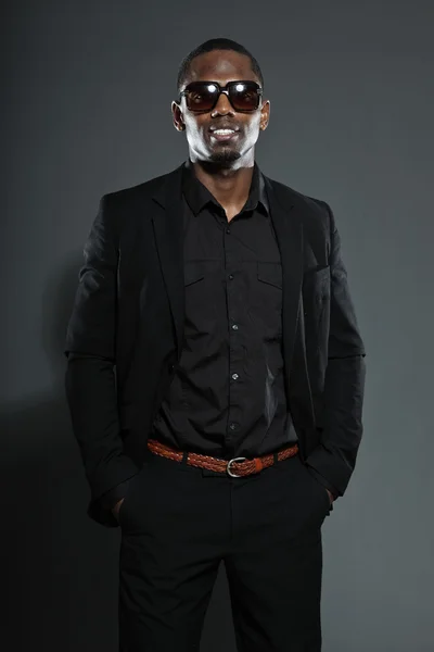 Hűvös, fekete amerikai férfi sötét öltöny. divat stúdió lövés elszigetelt a szürke háttér. sötét napszemüveget visel. — Stock Fotó