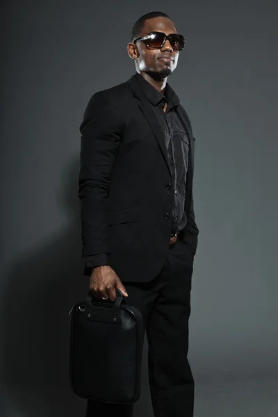 Hombre americano negro fresco en traje oscuro. Estudio de tiro de moda aislado sobre fondo gris. Usar gafas de sol oscuras . —  Fotos de Stock