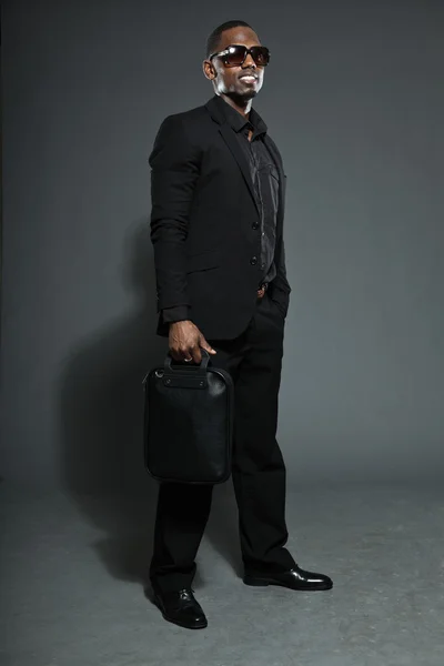 Hombre americano negro fresco en traje oscuro. Estudio de tiro de moda aislado sobre fondo gris. Usar gafas de sol oscuras . — Foto de Stock