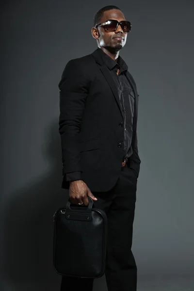 Freddo uomo nero americano in abito scuro. Studio moda girato isolato su sfondo grigio. Indossare occhiali da sole scuri . — Foto Stock