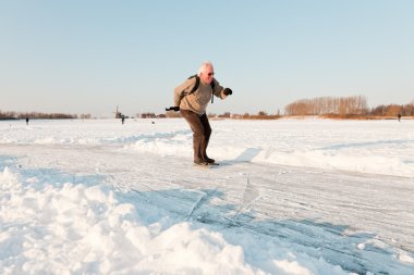 Dutch winter landscape with senior skater on frozen lake. Blue clear sky. Retired man. clipart