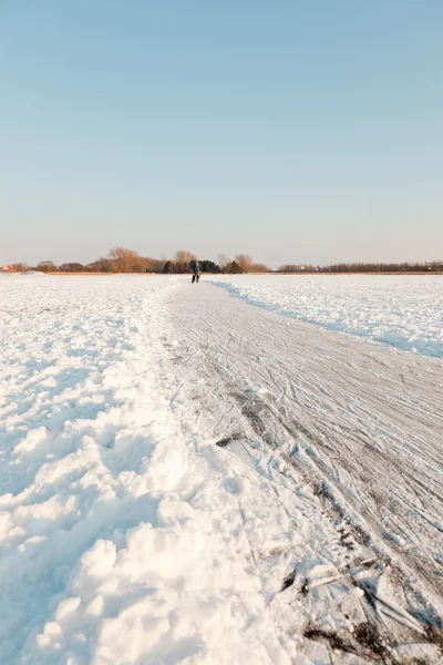 stock image Dutch winter landscape with skater on frozen lake. Blue clear sky.