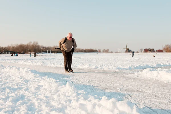 Dutch winter landscape with senior skater on frozen lake. Blue clear sky. Retired man. — Zdjęcie stockowe