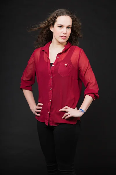 Menina bonita com cabelo encaracolado marrom longo. Retrato de estúdio de moda isolado contra fundo preto. Vestindo camisa vermelha . — Fotografia de Stock