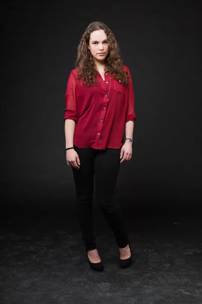 stock image Pretty girl with long brown curly hair. Fashion studio portrait isolated against black background. Wearing red shirt.