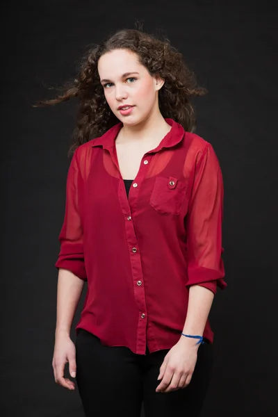 Mooi meisje met lange bruin krullend haar. mode studio portret geïsoleerd tegen zwarte achtergrond. het dragen van rode shirt. — Stockfoto