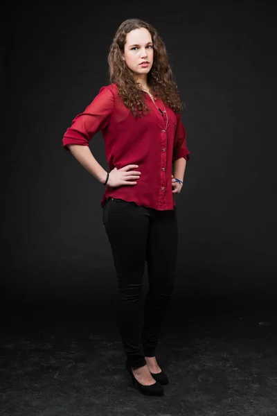 Pretty girl with long brown curly hair. Fashion studio portrait isolated against black background. Wearing red shirt. — Stock Photo, Image