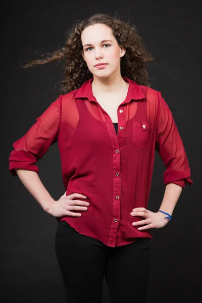 Söt flicka med långt brunt lockigt hår. mode studio porträtt isolerade mot svart bakgrund. Iklädd röd skjorta. — Stockfoto