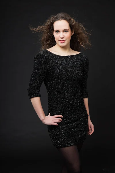 Hübsches Mädchen mit langen braunen lockigen Haaren. Modestudio Porträt isoliert vor schwarzem Hintergrund. trägt schwarzes Kleid. — Stockfoto