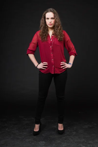 Pretty girl with long brown curly hair. Fashion studio portrait isolated against black background. Wearing red shirt. — Stock Photo, Image