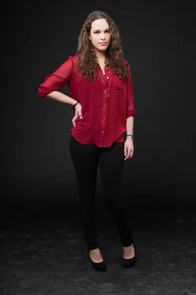 Söt flicka med långt brunt lockigt hår. mode studio porträtt isolerade mot svart bakgrund. Iklädd röd skjorta. — Stockfoto