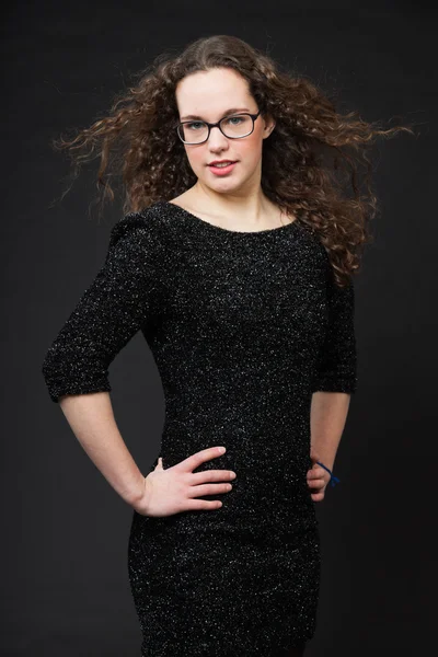 Όμορφο κορίτσι με μακριά καστανά σγουρά μαλλιά. στούντιο μόδας πορτρέτο που απομονώνεται ενάντια σε μαύρο φόντο. φορώντας γυαλιά και μαύρο φόρεμα. — Φωτογραφία Αρχείου