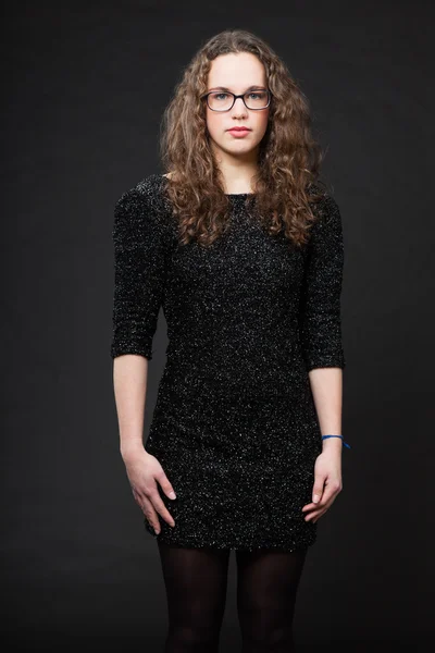 Hübsches Mädchen mit langen braunen lockigen Haaren. Modestudio Porträt isoliert vor schwarzem Hintergrund. trägt schwarzes Kleid und Brille. — Stockfoto