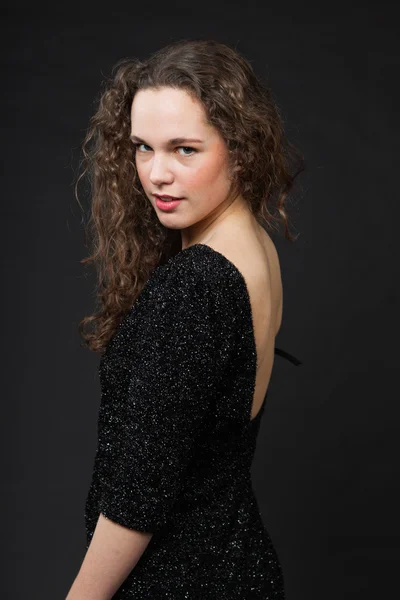 Pretty girl with long brown curly hair. Fashion studio portrait isolated against black background. Wearing black dress. — Stock Photo, Image