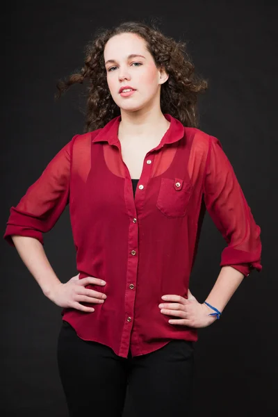 Bella ragazza con lunghi capelli castani ricci. Ritratto di studio di moda isolato su sfondo nero. Indossare camicia rossa . — Foto Stock