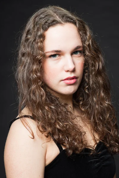 Pretty girl with long brown curly hair. Fashion studio portrait isolated against black background. Wearing black dress. — Stock Photo, Image