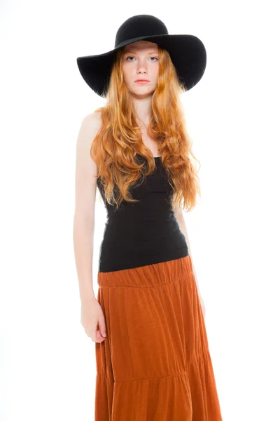 Bella ragazza con lunghi capelli rossi che indossa camicia nera e abito marrone e cappello nero. Studio di moda girato isolato su sfondo bianco . — Foto Stock