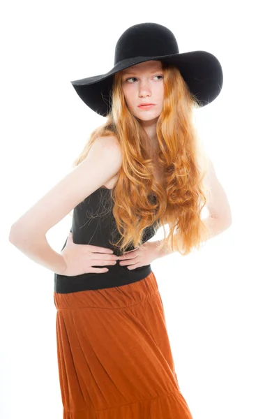 Chica guapa con el pelo largo y rojo vistiendo camisa negra y vestido marrón y sombrero negro. Estudio de moda tiro aislado sobre fondo blanco . — Foto de Stock
