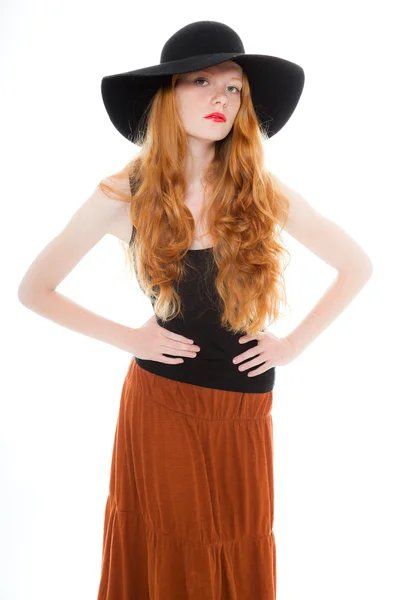 Menina bonita com cabelos longos ruivos vestindo camisa preta e vestido marrom e chapéu preto. Estúdio de moda tiro isolado no fundo branco . — Fotografia de Stock