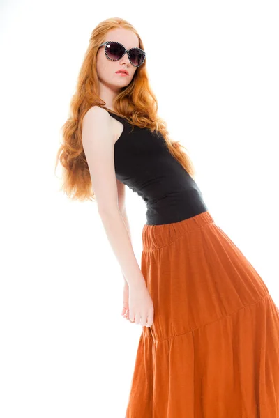 Pretty girl with long red hair wearing black shirt and brown dress and retro sunglasses. Fashion studio shot isolated on white background. — Stock Photo, Image