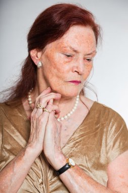 Portrait of good looking senior woman with expressive face showing emotions. Thinking and hoping. Acting young. Studio shot isolated on grey background. clipart