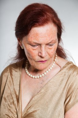 Portrait of good looking senior woman with expressive face showing emotions. Thinking and hoping. Acting young. Studio shot isolated on grey background. clipart