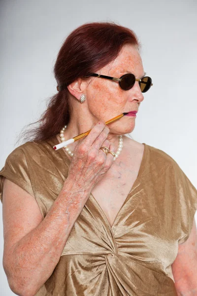 Portret van goed uitziende senior vrouw met expressief gezicht toont emoties. dragen van een zonnebril en roken van een sigaret. handelend jonge. studio opname geïsoleerd op grijze achtergrond. — Stockfoto