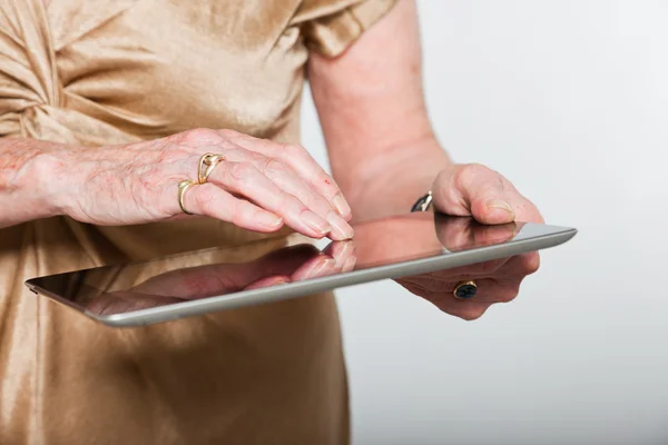Mãos de uma mulher idosa usando um tablet. Estúdio filmado em fundo cinza . — Fotografia de Stock