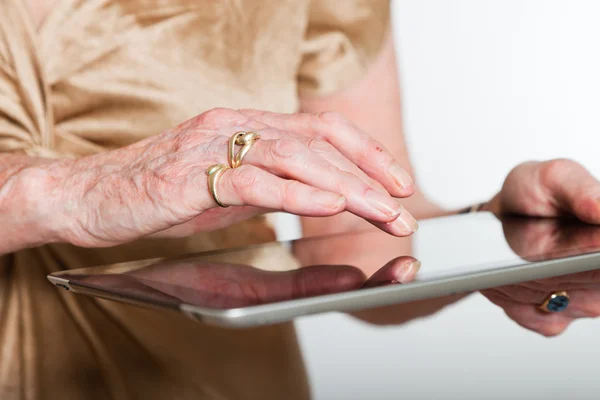 Händerna på en äldre kvinna med en tablett. Studio skott på grå bakgrund. — Stockfoto