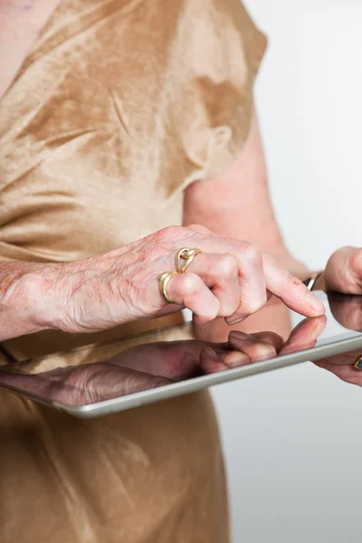 Manos de una mujer mayor usando una tableta. Estudio sobre fondo gris . — Foto de Stock