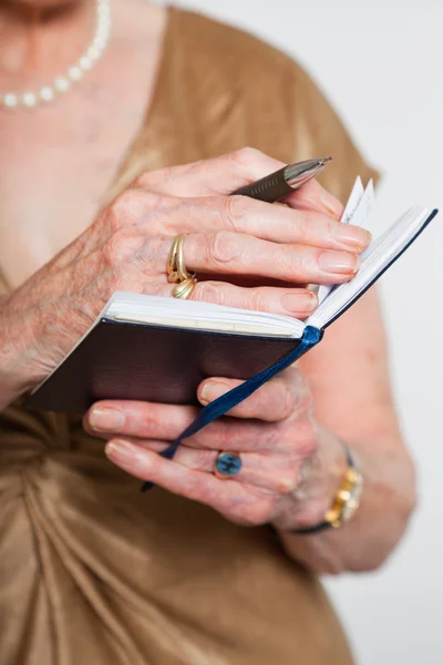 Les mains d'une femme âgée qui tient un agenda. Studio tourné sur fond gris . — Photo