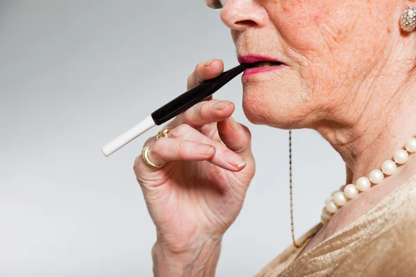 Nahaufnahme einer Seniorin, die eine Zigarette raucht. Studioaufnahme auf grauem Hintergrund. — Stockfoto