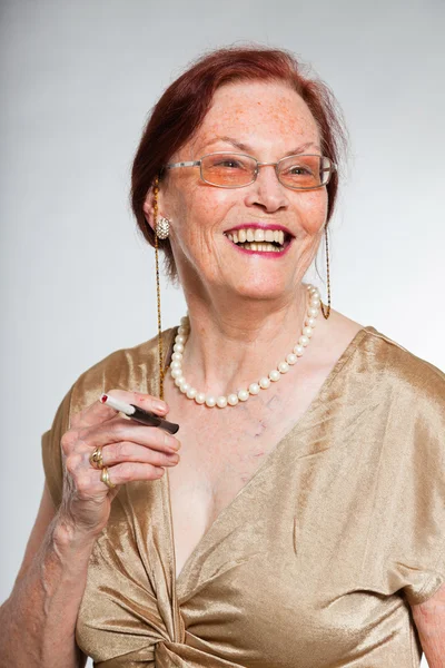 Портрет добродушної старшої жінки в окулярах з виразним обличчям, що демонструє емоції. Палити цигарку. Поводитися молодо. Студійний знімок ізольовано на сірому фоні . — стокове фото