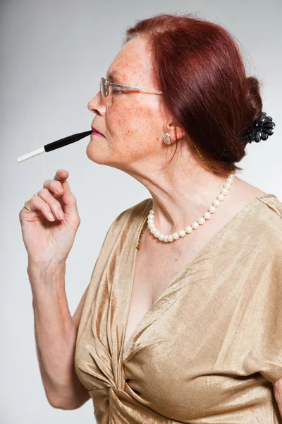 Retrato de una mujer mayor guapa usando gafas con cara expresiva mostrando emociones. Fumar un cigarrillo. Actuando joven. Estudio plano aislado sobre fondo gris . — Foto de Stock