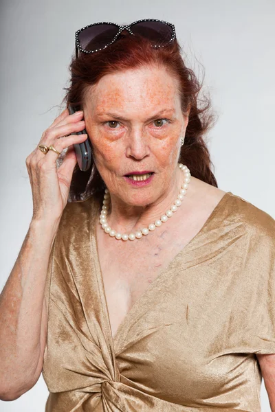Портрет красивой пожилой женщины с выразительным лицом, выражающим эмоции. Звоню с мобильного. Молодость. Съемка изолирована на сером фоне . — стоковое фото
