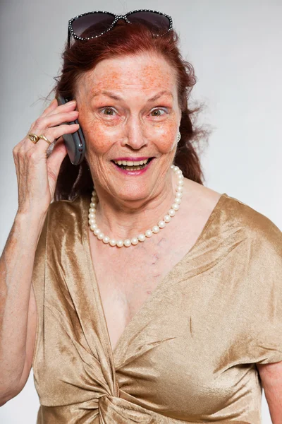 Ritratto di bella donna anziana con volto espressivo che mostra emozioni. Chiamo con il cellulare. Si comporta da giovane. Studio girato isolato su sfondo grigio . — Foto Stock