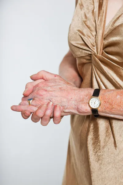 Närbild av händerna på äldre kvinna som bär en klocka och ring. Studio skott isolerade på grå. — Stockfoto