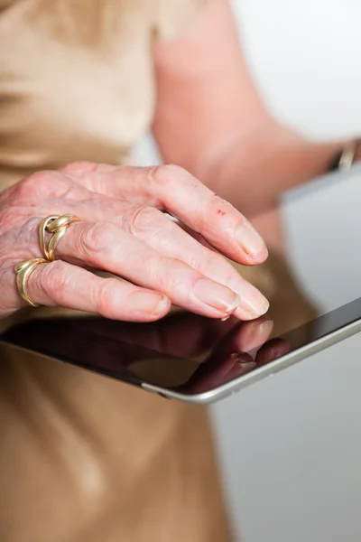 Händerna på en äldre kvinna med en tablett. Studio skott på grå bakgrund. — Stockfoto