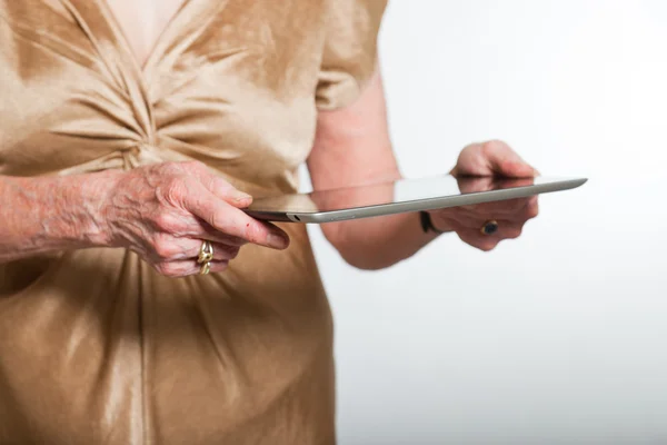 Ruce starší ženy pomocí tablet. Studio záběr na šedém pozadí. — Stock fotografie