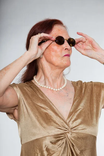 Ritratto di bella donna anziana che indossa occhiali da sole con viso espressivo che mostra emozioni. Si comporta da giovane. Studio girato isolato su sfondo grigio . — Foto Stock