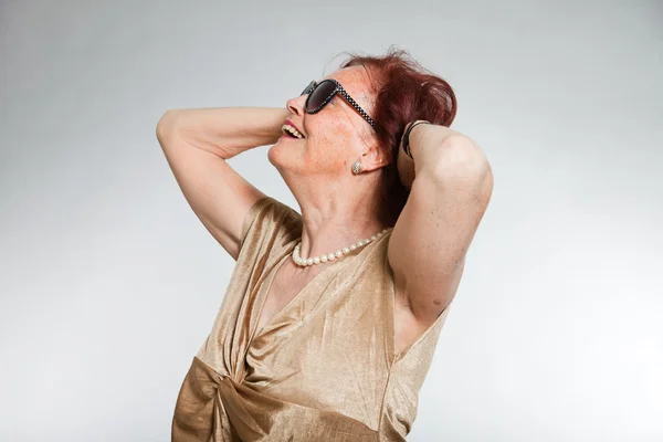 Porträtt av bra senior kvinna bär solglasögon med uttrycksfulla ansikte visar känslor. glad och fri. agerar unga. Studio skott isolerade på grå bakgrund. — Stockfoto