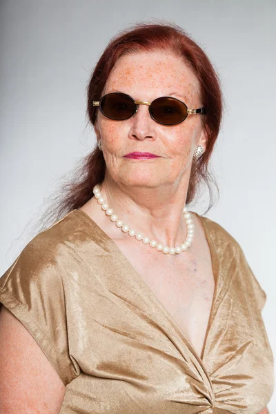 Portret van goed uitziende senior vrouw dragen van een zonnebril met expressief gezicht toont emoties. handelend jonge. studio opname geïsoleerd op grijze achtergrond. — Stockfoto