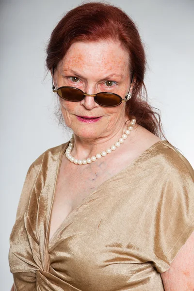 Портрет добродушної старшої жінки в сонцезахисних окулярах з виразним обличчям, що демонструє емоції. Поводитися молодо. Студійний знімок ізольовано на сірому фоні . — стокове фото